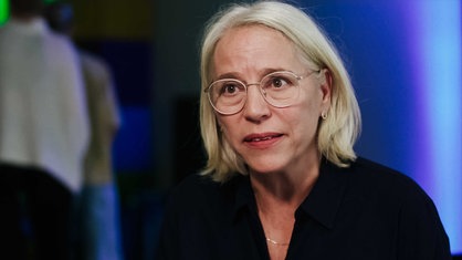Anje Mies, kurze blond-weiße Haare, gold-umrandetet Brille, dunkel-blaue Bluse