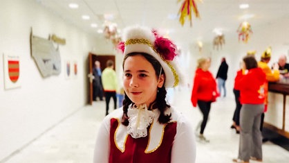 Vanessa Buch steht kostümiert als Tanzmariechen in einem Raum das Karnevalsverein. Im Hintergrund sind unscharf mehrere Leute zu erkennen. 