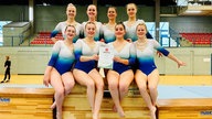 Eine Gruppe junger Frauen, die alle den gleichen Turnanzug tragen und mit einer Urkunde posieren.