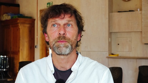 Matthias Bäcker sitzt auf einem Stuhl und schaut betroffen nach oben.