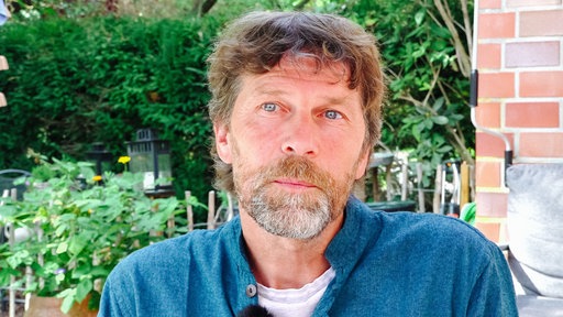 Matthias Bäcker sitzt im Garten unter einer Überdachung. Sein Blick wirkt betroffen.