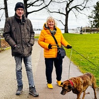 Stefan Becker und Monika Keiler, ein Mann und eine Frau mittleren Alters, spazieren mit zwei Hunden im Park.