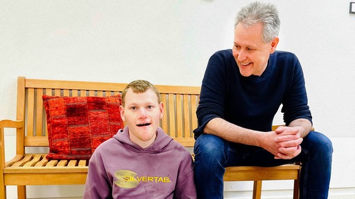Zwei Männer, einer sitzt auf einer Bank, der andere davor
