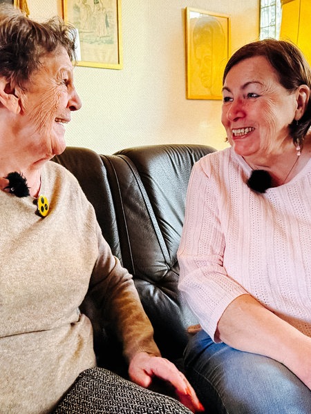 Zwei Frauen sitzen auf einem Sofa und lachen sich an