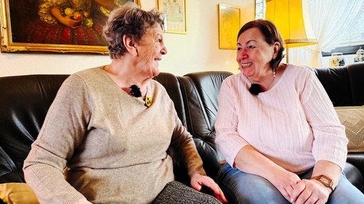 Zwei Frauen sitzen auf einem Sofa und lachen sich an