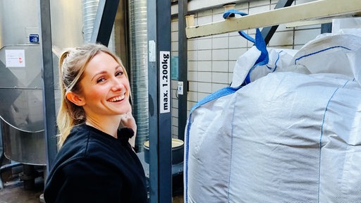 Lena Backes, eine junge Frau, steht neben einem riesigen Sack voll Malz.