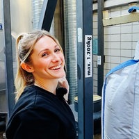 Lena Backes, eine junge Frau, steht neben einem riesigen Sack voll Malz.