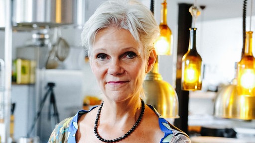 Angela von der Goltz von Nahem fotografiert. Hinter ihr hängen zwei verzierte Glühbirnen von der Decke.