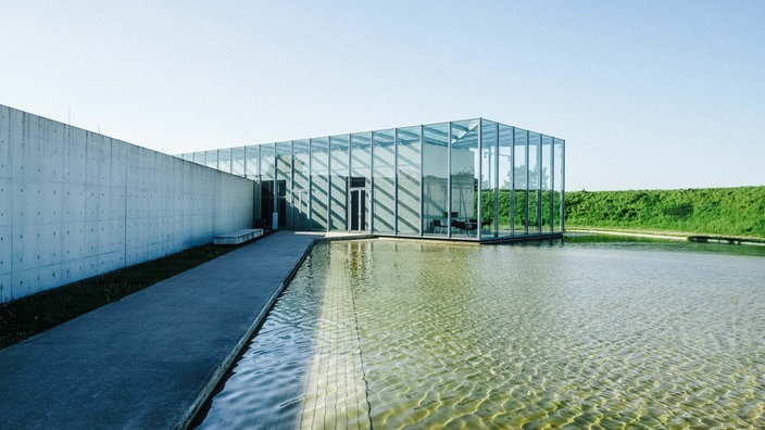 Ein langer Glasbau, der auf einen künstlich angelegten Teich ragt.