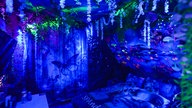 In blaues Licht getauchtes Zimmer mit Bett udn Tisch, an den Wänden und der Decke Natur-Symole wie Schmetterlinge und Pilze, von der Decke hängen künstliche Pflanzen 