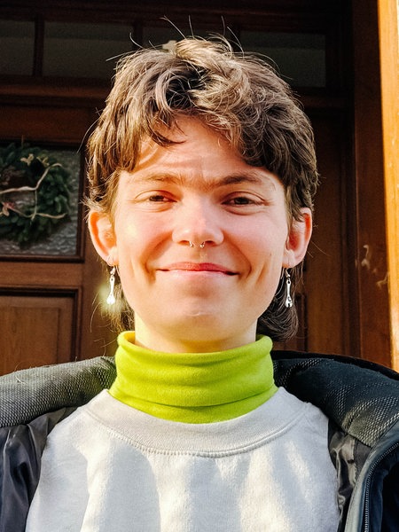 Das Portrait einer Frau, im Hintergrund die Fassade eines Hauses
