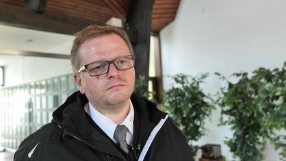 Portrait von Bestatter Roman Vosskühler, ein Mann mit kurzen, blonden Haaren und Brille.