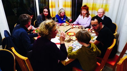Eine Gruppe von Menschen in unterschiedlichen Altersstufen sitzen gemeinsam an einem Tisch und essen