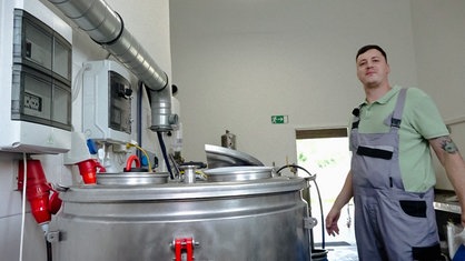 Philipp Löffler stet in Latzhose neben einem großen Biertank in seiner Braustube.