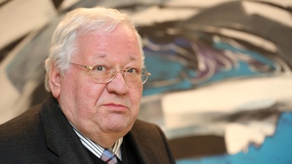 Manfred Becker-Huberti, ein älterer Mann mit kurzen weißen Haaren und Brille im Anzug, lächelt.