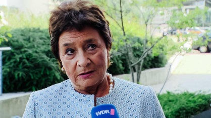 Hannelore Rönsch, kurze braune Haare, Perlen-Ohrringe und Perlen-Kette, hellblaues Kostüm, spricht in ein WDR-Mikrofon