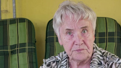 Helga Ladek, eine 85-jährige Frau mit grauen kurzen Haaren und grünen Augen, blickt direkt in die Kamera. 