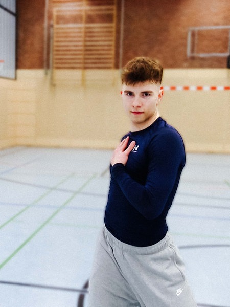 Tänzer Christian Weiß steht mit einer Hand auf der Brust in einer Turnhalle und schaut in die Kamera.