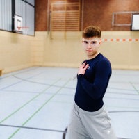 Tänzer Christian Weiß steht mit einer Hand auf der Brust in einer Turnhalle und schaut in die Kamera.