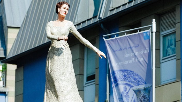 Die Skulptur einer Frau im Brautkleid steht auf einer Litfaßsäule.