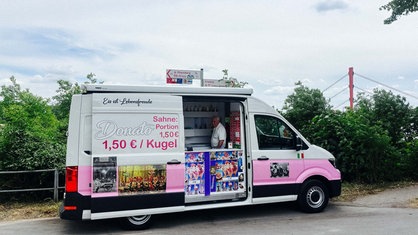 Ein weiß-pinker Eiswagen vor grünen Büschen