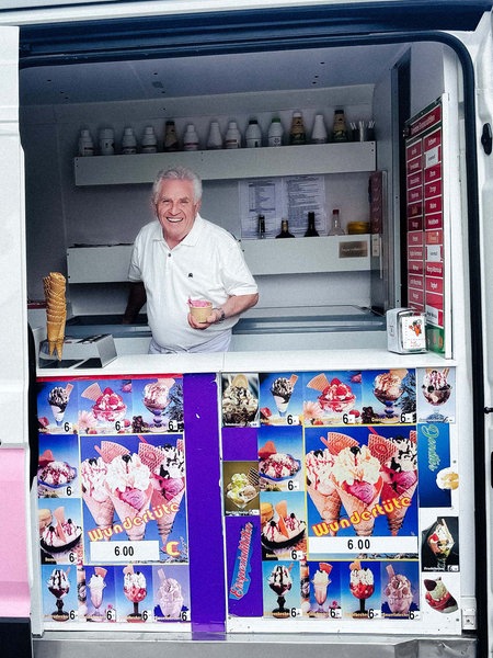 Ein Mann steht in einem weiß-pinken Eiswagen und hält Eis in der Hand