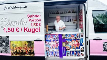 Ein Mann steht in einem weiß-pinken Eiswagen und hält Eis in der Hand