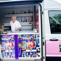 Ein Mann steht in einem weiß-pinken Eiswagen und hält Eis in der Hand