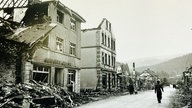 Eine Straße voller zerstörter Häuser, nur die Fassaden stehen noch, am Straßenrand sind Trümmer aufgehäuft