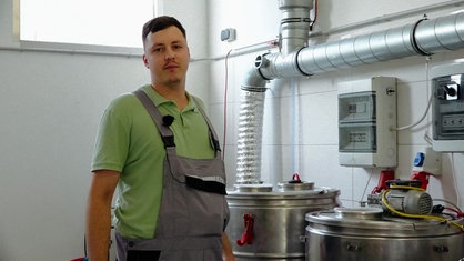 Philipp Löffler in Arbeitskleidung in seiner Braustube, neben ihm stehen silberne Behälter.