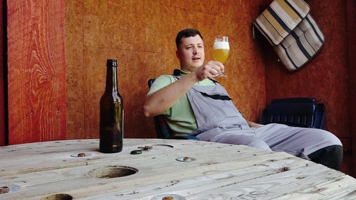 Philipp Löffner sitzt im Garten auf einem Stuhl und hält ein Glas mit Bier in der Hand.