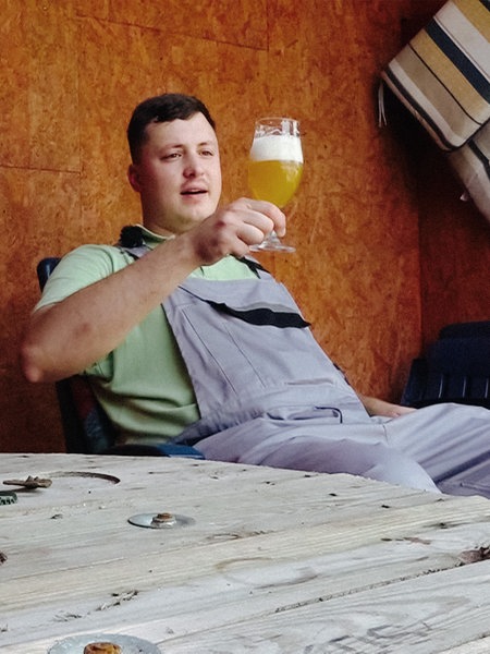 Philipp Löffner sitzt im Garten auf einem Stuhl und hält ein Glas mit Bier in der Hand.