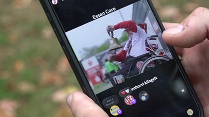 Eine Person hält ein Handy in der Hand, auf dem Display ist ein Video des verstorbenen Rot-Weiss Essen-Fans "Glockenhorst" zu sehen.