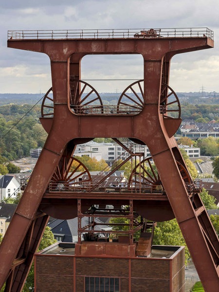 Der Doppelblock der Zeche Zollverein in Essen, dahinter ein weiter Blick über Häuser und Bäume in der Stadt.
