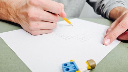 Aufnahme einer Hand, die einen Bleistift hält und auf ein weißes Papier malt