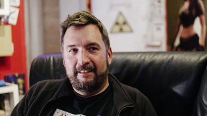 Jan Stermann sitzt in Tino Menzners Gaming-Keller. Er lächelt.