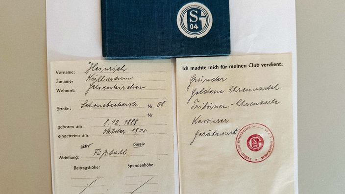 Das aufgeschlagene Mitgliedsheft von Heinrich Kullmann. Darüber liegt ein Buch mit dem Schalke-Logo.