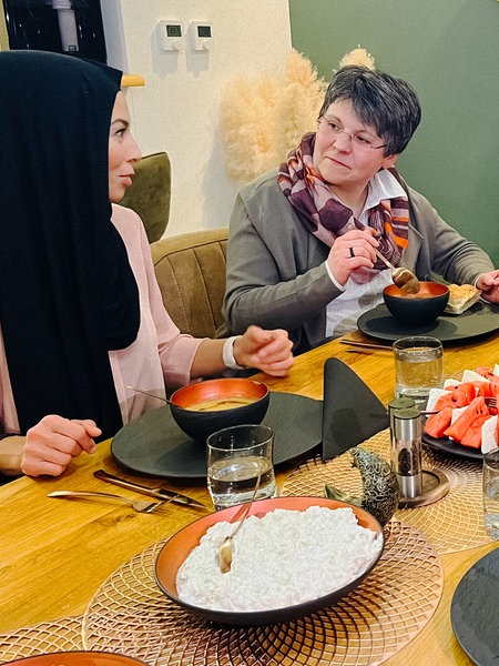 Einige Personen unterschiedlichen Alters sitzen an einem Tisch. Auf dem Tisch befindet sich Essen
