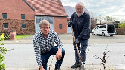 Antonius Brinkhaus und Franz Pieper vom "Hackeclub" setzen eine neue Hecke. Pieper hält eine Schaufel in der Hand, Brinkhaus kniet neben ihm.