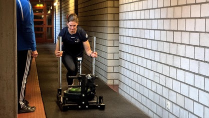 Neele Schuten, eine junge Frau, schiebt einen schweren Traininsschlitten über den Boden.