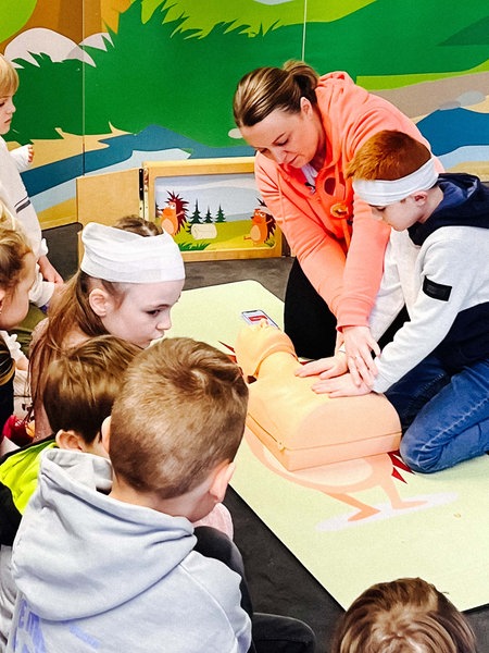 Eine Frau erklärt einer Gruppe von Kindern wie eine Herz-Rhythmus-Massage funktioniert.