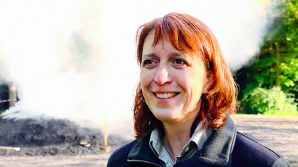 Juliane Saebel vom RVR Grün vor dem qualmenden Kohlemeiler. Sie lächelt.