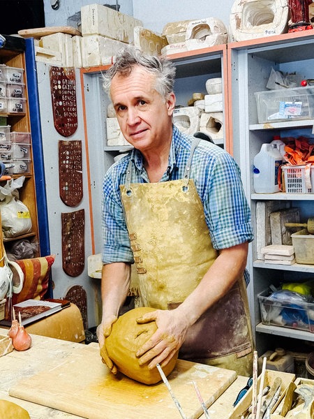 Paul Weynans steht in seiner Werkstatt, er trägt eine Schürze und arbeitet an einem großen Klumpen Ton.