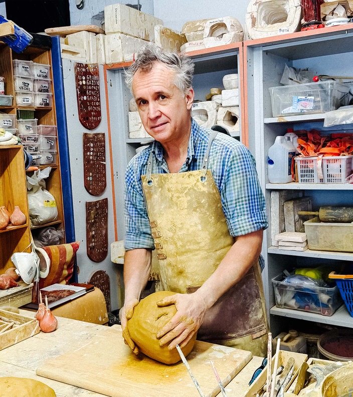 Paul Weynans steht in seiner Werkstatt, er trägt eine Schürze und arbeitet an einem großen Klumpen Ton.