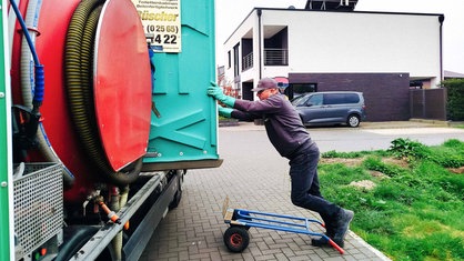 Berni Bösing schiebt eine Toilettenkabine auf eine Ladefläche von einem Lkw.