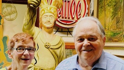 Ein Mann und eine Frau blicken in die Kamera, hinter ihnen eine Statue.