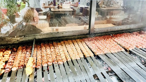 Auf einem Holzkohlegrill liegen über 30 Fleischspieße.