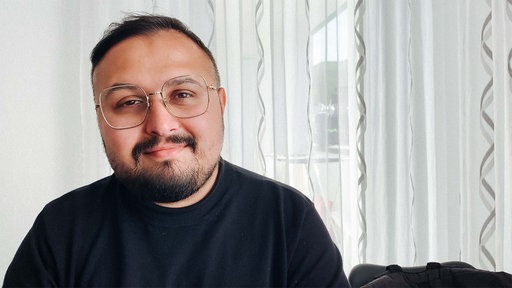 Ilia Vasilev, ein Mann mit kurzen schwarzen Haaren, Bart und Brille, lächelt in die Kamera.