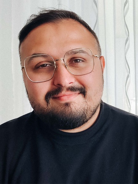 Ilia Vasilev, ein Mann mit kurzen schwarzen Haaren, Bart und Brille, lächelt in die Kamera.