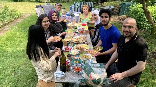 Mehrere Menschen sitzen beim Picknick im gemeinsamen Garten